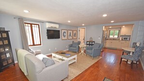 A living room with a sofa, armchairs, a coffee table, and a TV. There is a kitchen area with cabinets and a microwave. - Charming, Updated Home in the Heart of Downtown Glen Arbor!  (Glen Arbor)