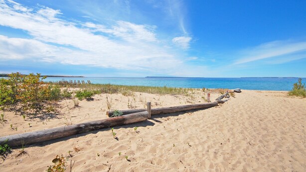 A sandy beach with a wooden log barrier and sparse vegetation. - Charming, Updated Home in the Heart of Downtown Glen Arbor!  (Glen Arbor)