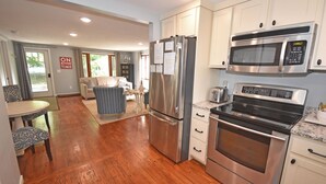 A modern kitchen with stainless steel appliances, a dining area with patterned chairs, and a living room with a sofa and curtains. - Charming, Updated Home in the Heart of Downtown Glen Arbor!  (Glen Arbor)