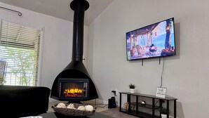 Olohuoneessa on musta puukamiina, seinälle asennettu televisio, musta sohvapöytä ja kirjahylly.
