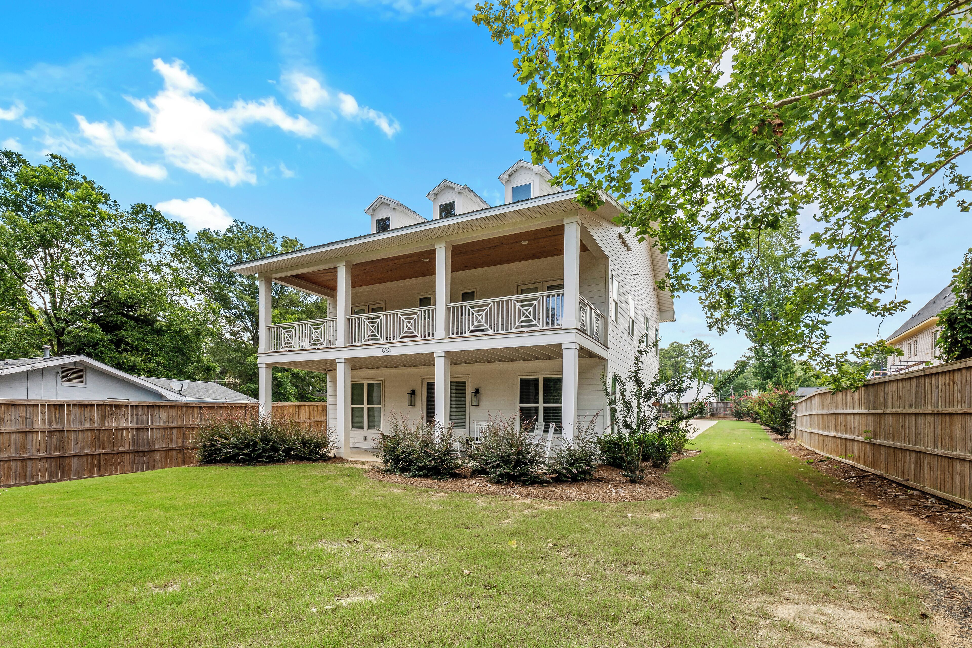 A two-story house with a balcony, surrounded by a wooden fence and a well-maintained lawn.