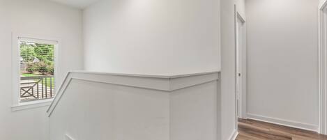 A clean, white-walled stairwell with a wooden floor, leading to a door.