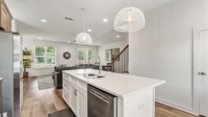 Cocina moderna con armarios blancos, una isla central con pileta y electrodomésticos de acero inoxidable, e iluminación colgante.