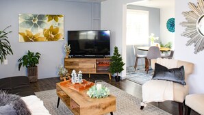 A living room with a flat-screen TV, wooden coffee table, and a beige sofa. - Stay near Point Defiance Park in our charming 1-bedroom cottage (Tacoma)
