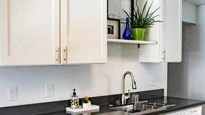 A modern kitchen with white cabinets, a black countertop, stainless steel appliances, and a hanging light fixture. - Stay near Point Defiance Park in our charming 1-bedroom cottage (Tacoma)