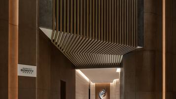 A modern hotel lobby with a sleek, minimalist design, featuring a central column, a reception desk, and a distinctive ceiling pattern.