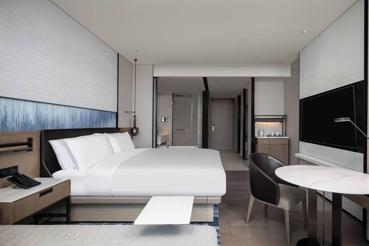 Une chambre d’hôtel moderne dotée d’un grand lit, d’un bureau avec un ordinateur, d’une télévision et d’un petit coin salon.