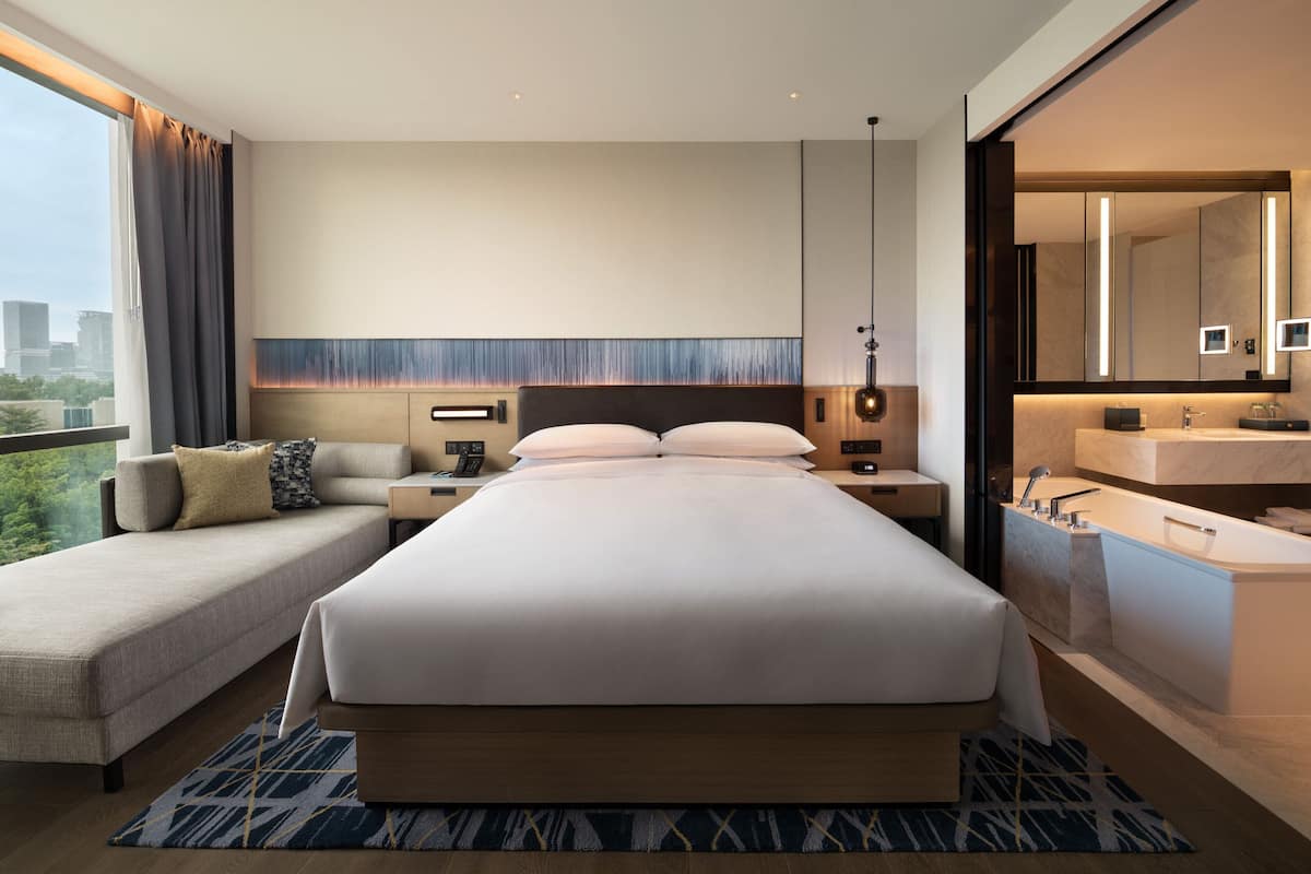 Une chambre d’hôtel moderne dotée d’un grand lit, d’un canapé, d’un bureau, d’une table de chevet, d’une salle de bain avec baignoire et offrant une vue sur la ville.