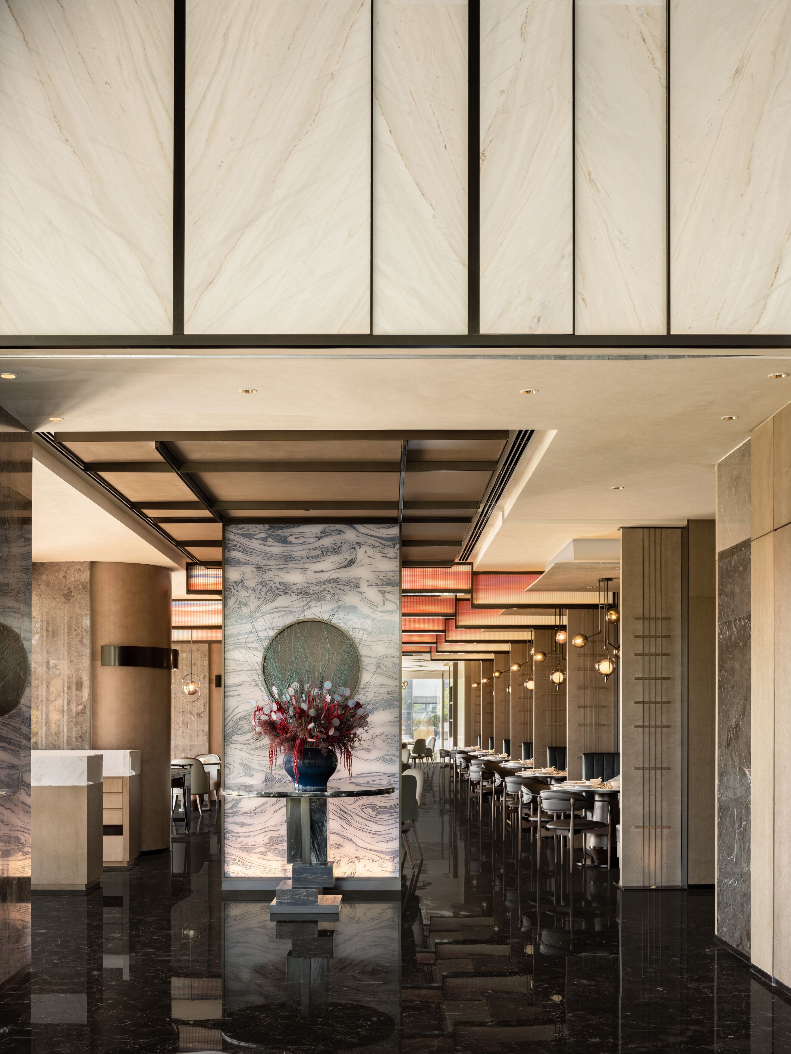 A modern hotel lobby with marble walls, a central column with a vase, and a dining area with tables and chairs.