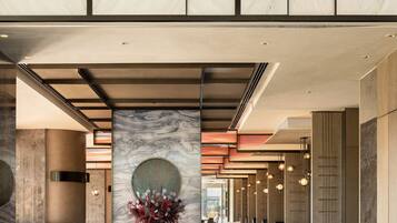A modern hotel lobby with marble walls, a central column with a vase, and a dining area with tables and chairs.