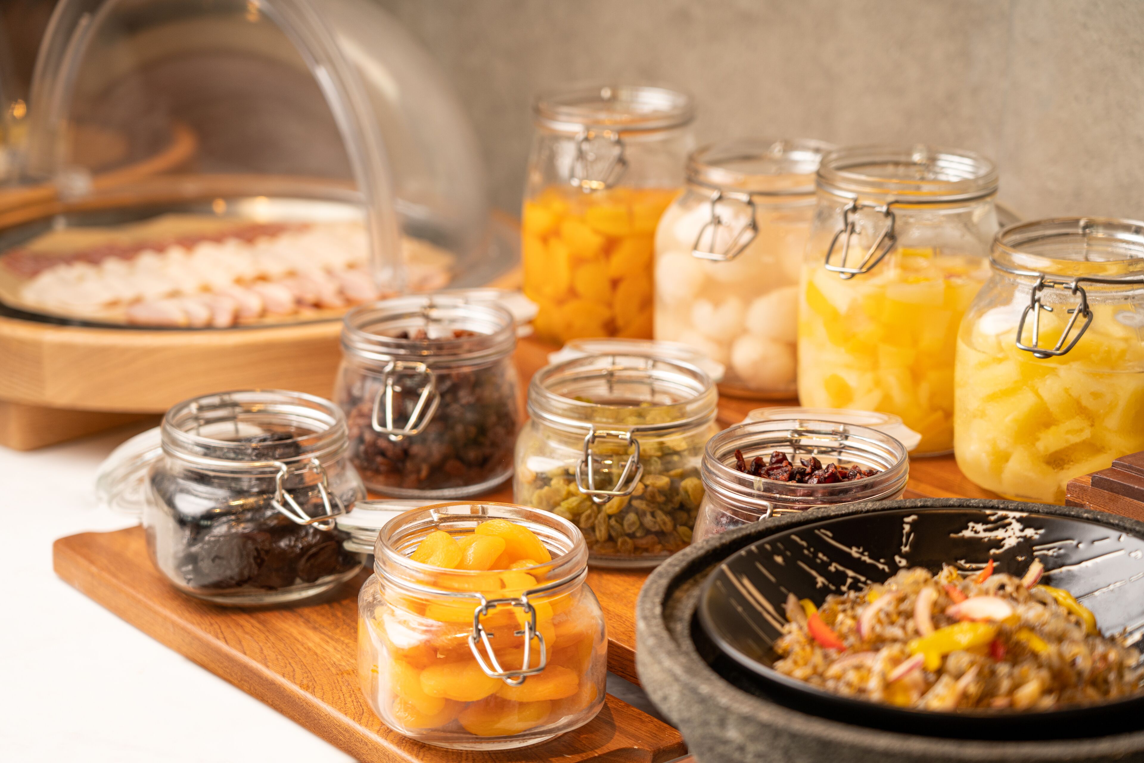 A buffet with various food items in glass jars and a bowl of mixed vegetables.