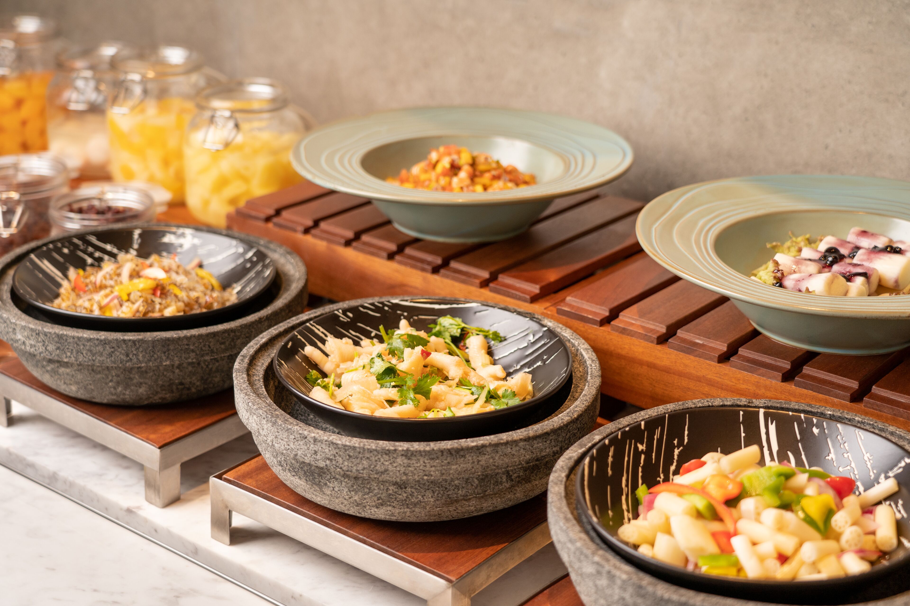 A buffet with various dishes in stone bowls on wooden stands.