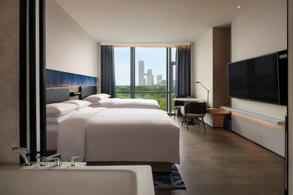 Une chambre d’hôtel moderne avec deux lits, une grande télévision et une vue sur la ville.