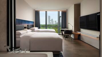 A modern hotel room with two beds, a large TV, and a city view.