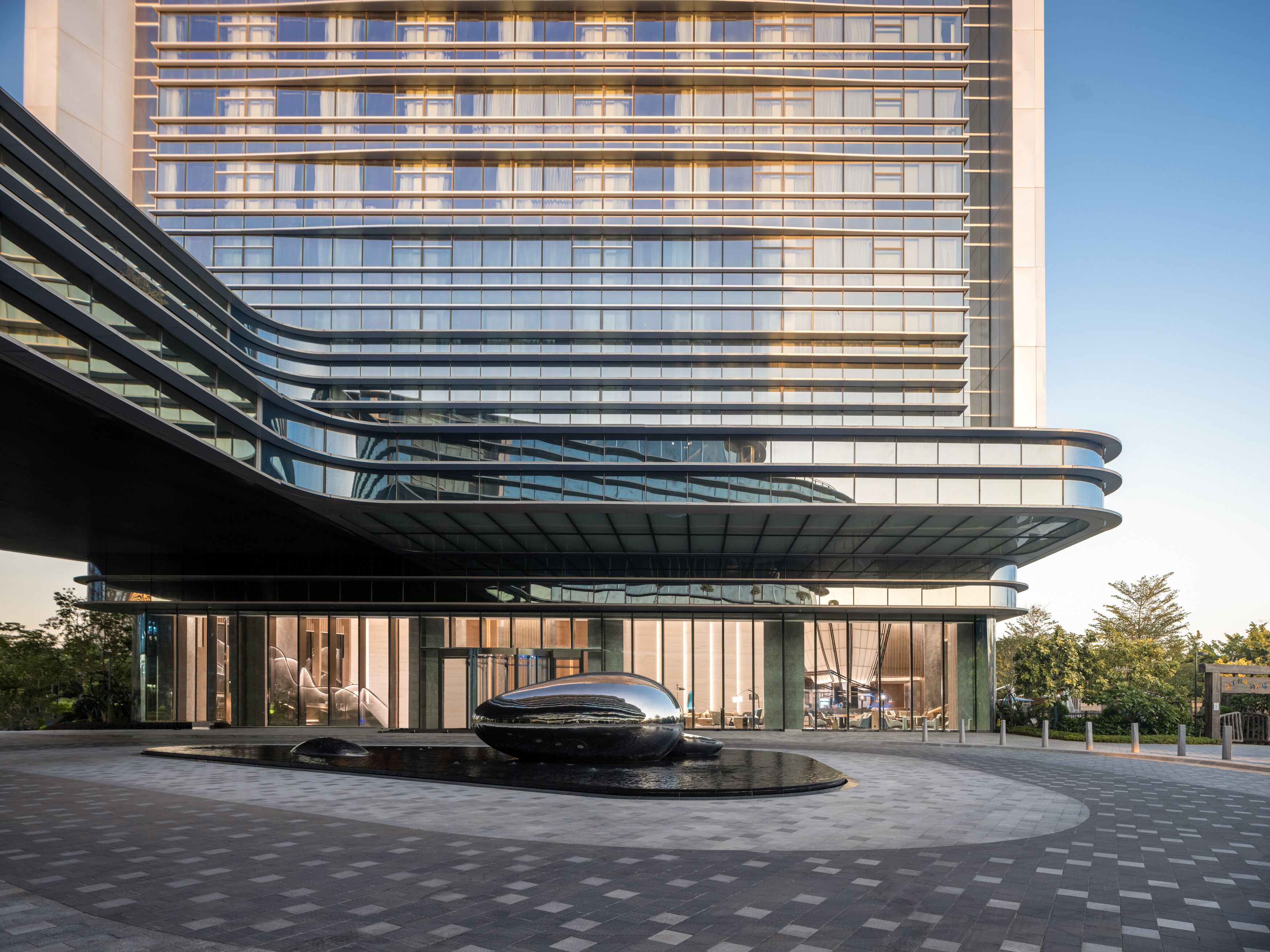 A modern building with a curved glass facade and a reflective water feature in front.
