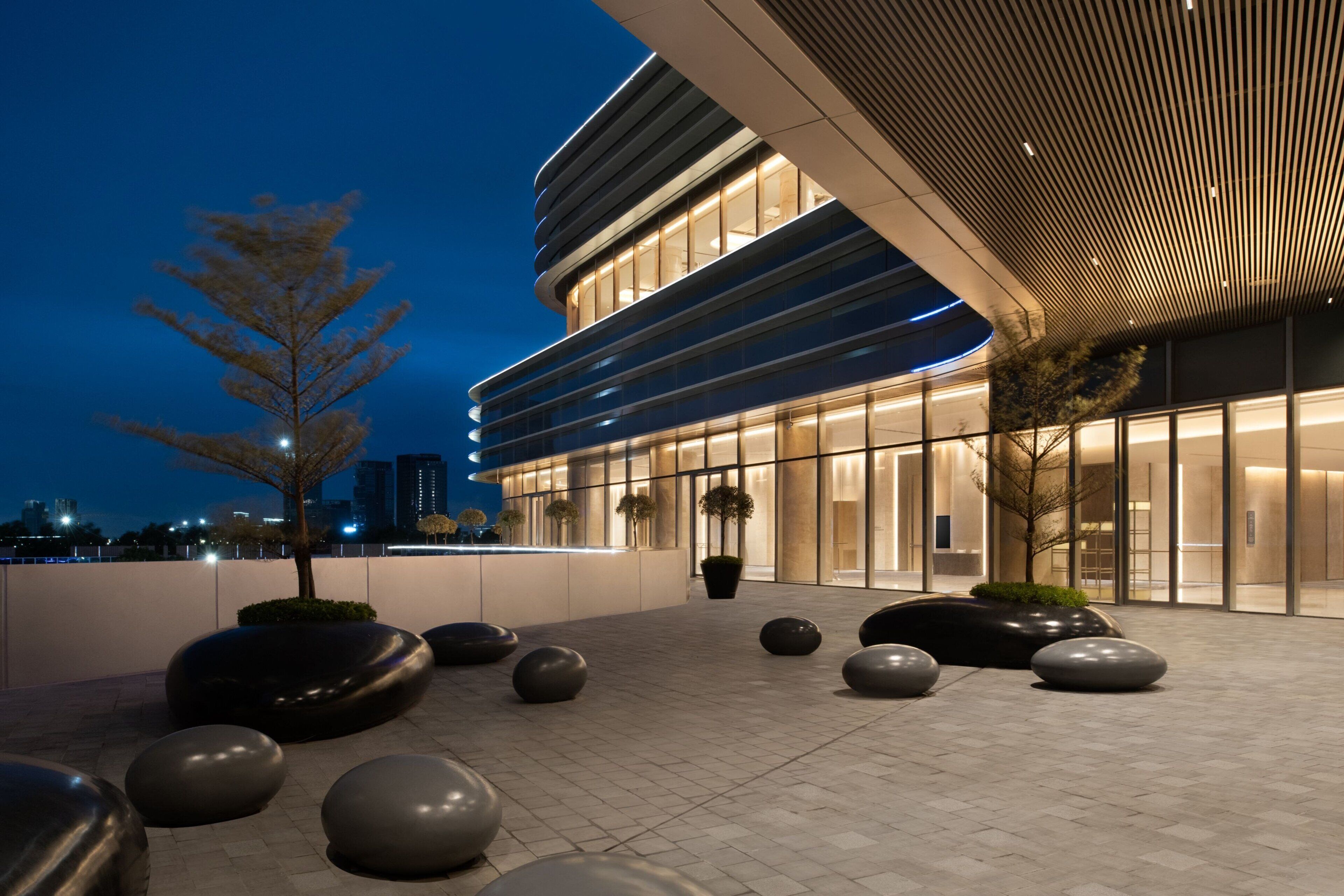 An outdoor area with modern architecture, including a building with large windows and a curved roof, surrounded by spherical seating and a few trees.