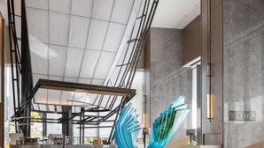 Un vestíbulo moderno con una gran escultura abstracta, zonas de estar y vistas al exterior.