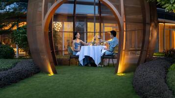 Un comedor con una mesa dispuesta para tres personas, rodeado por una estructura semicircular con paredes de vidrio.