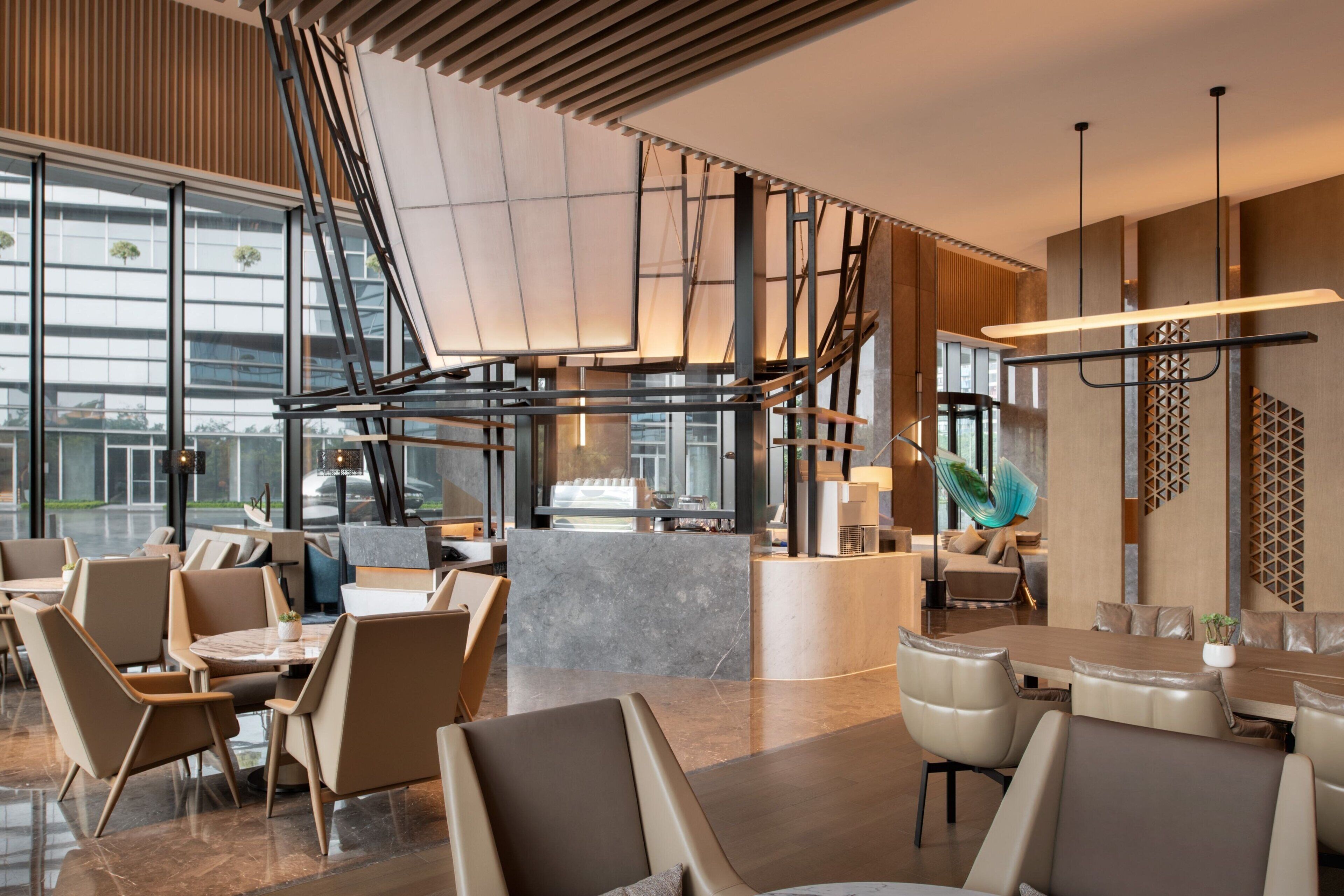 Un interior moderno con una zona de estar central, una escalera y ventanas amplias.