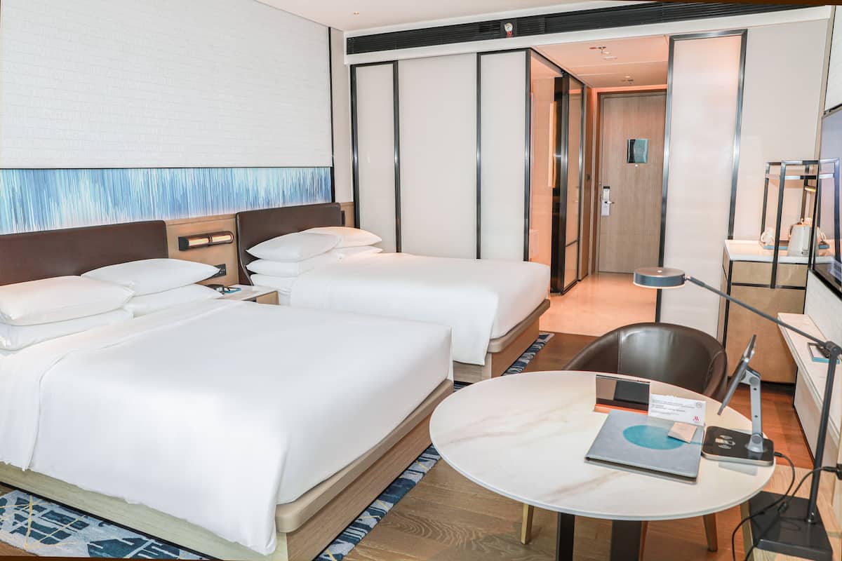 Une chambre d’hôtel avec deux lits, une table ronde avec un ordinateur portable et un bureau avec une lampe.