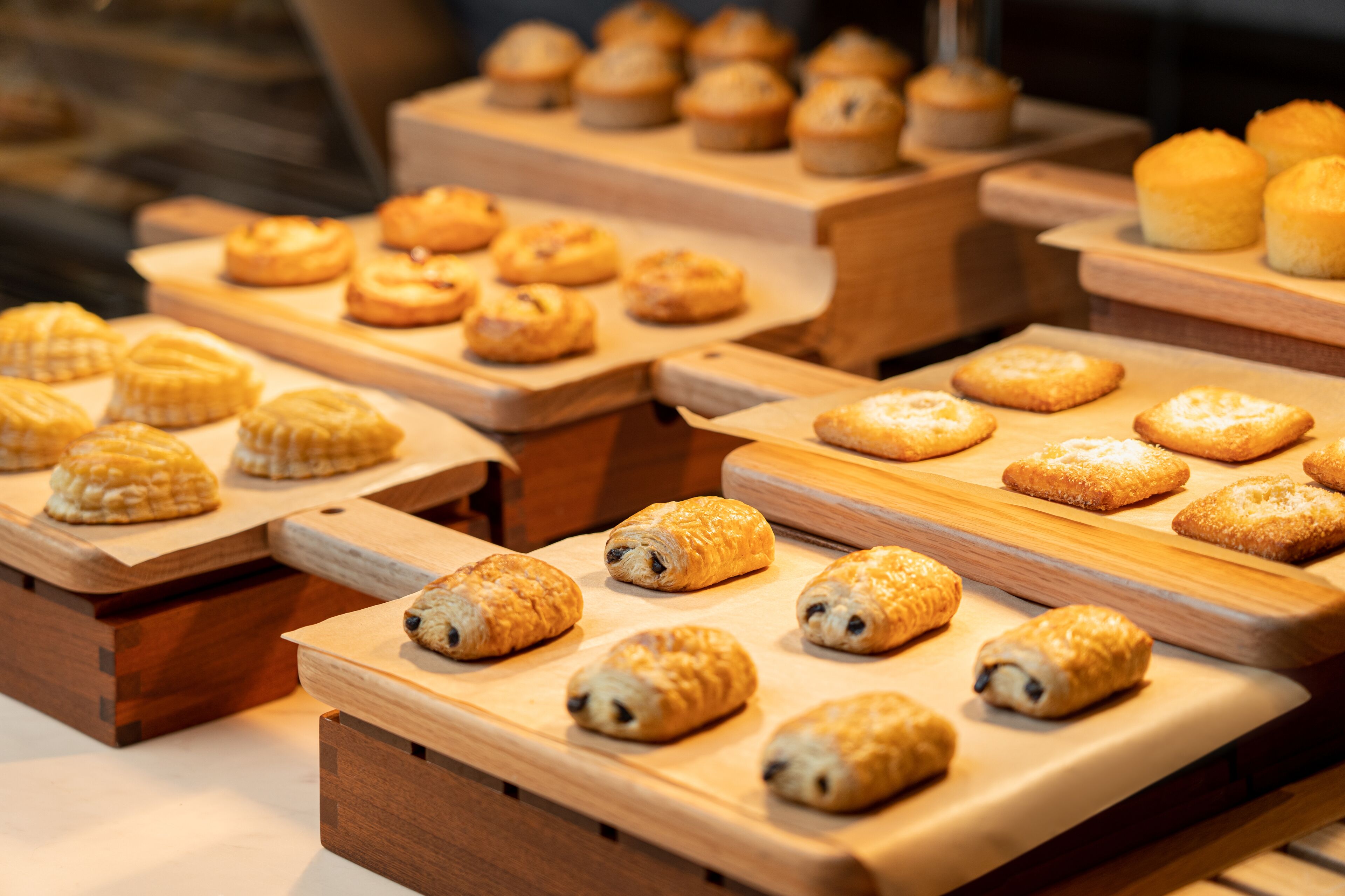 Une variété de pâtisseries présentées sur des planches en bois dans une boulangerie.