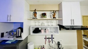 A compact kitchen with white cabinets, a black range hood, and shelves with decorative items and kitchenware.