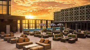 An outdoor seating area with multiple couches and tables, a pool in the background, and a sunset sky. - Le Méridien Taichung (Taichung)