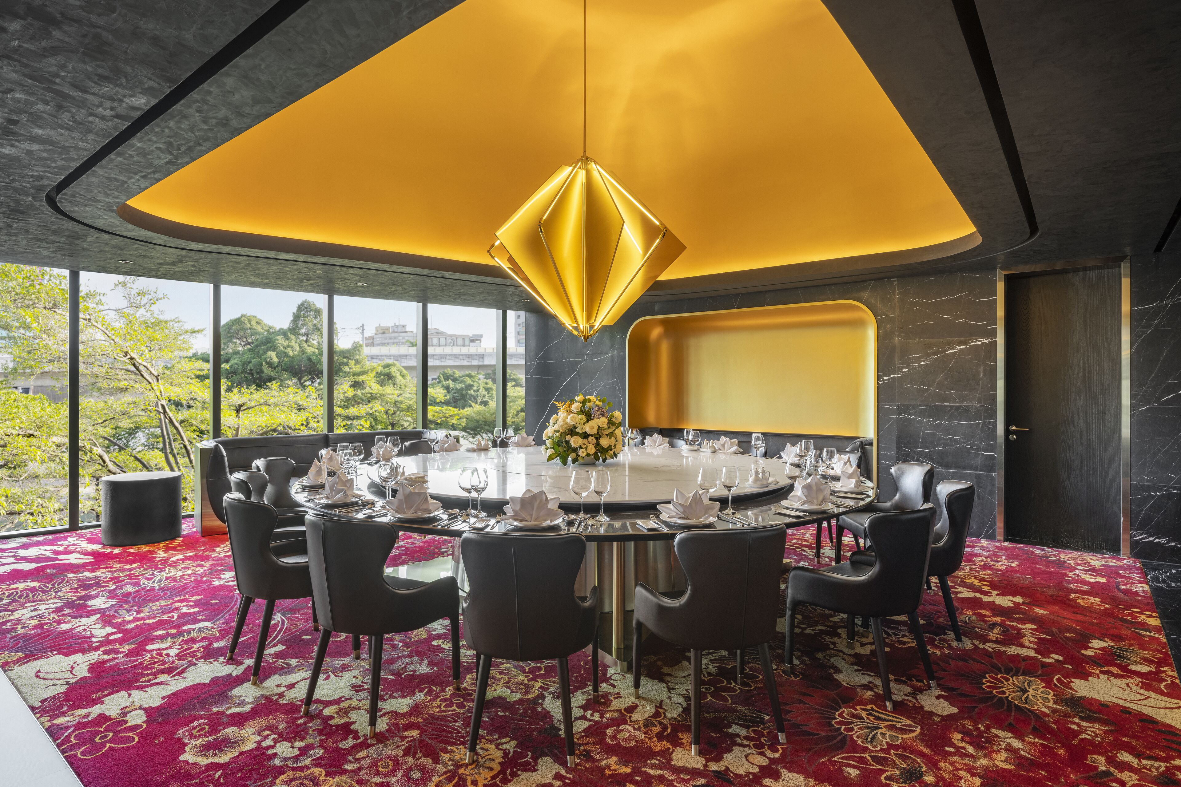 A modern dining room with a round table set for six, black chairs, and a yellow pendant light.