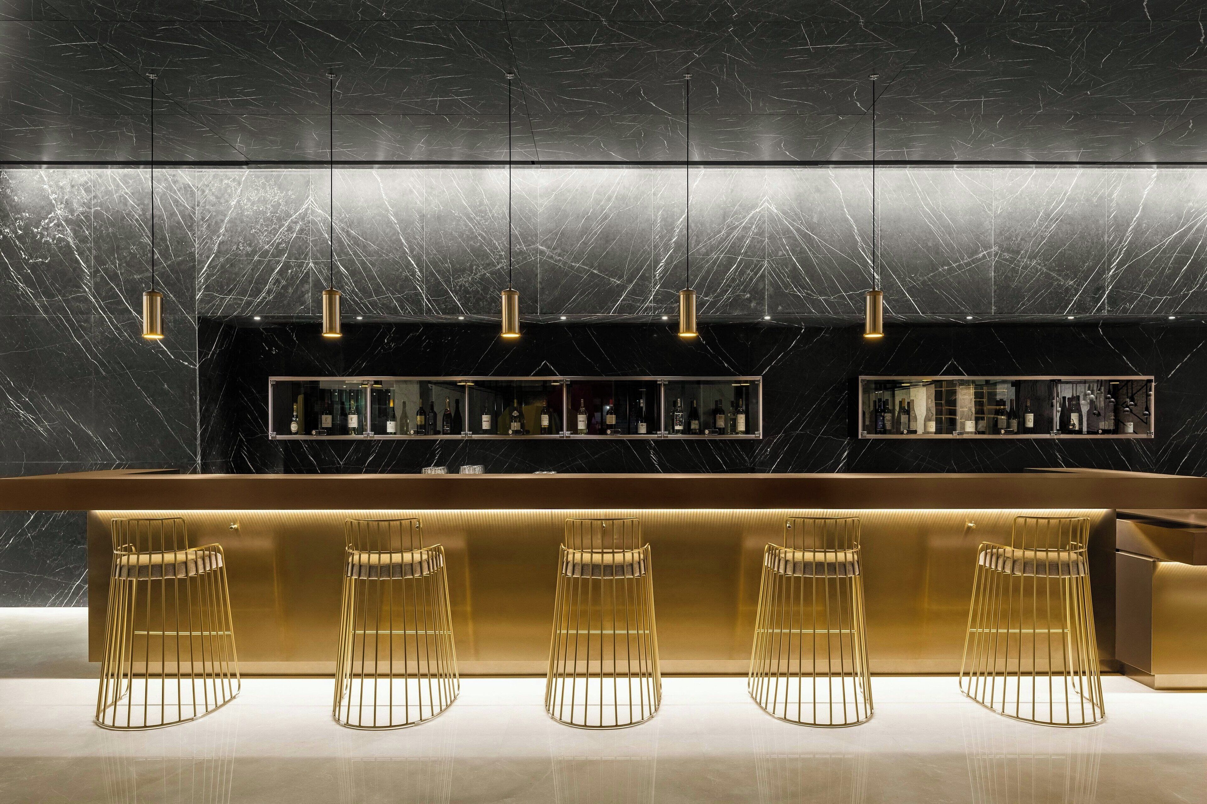 A modern bar area with a marble countertop, gold bar stools, and pendant lighting.