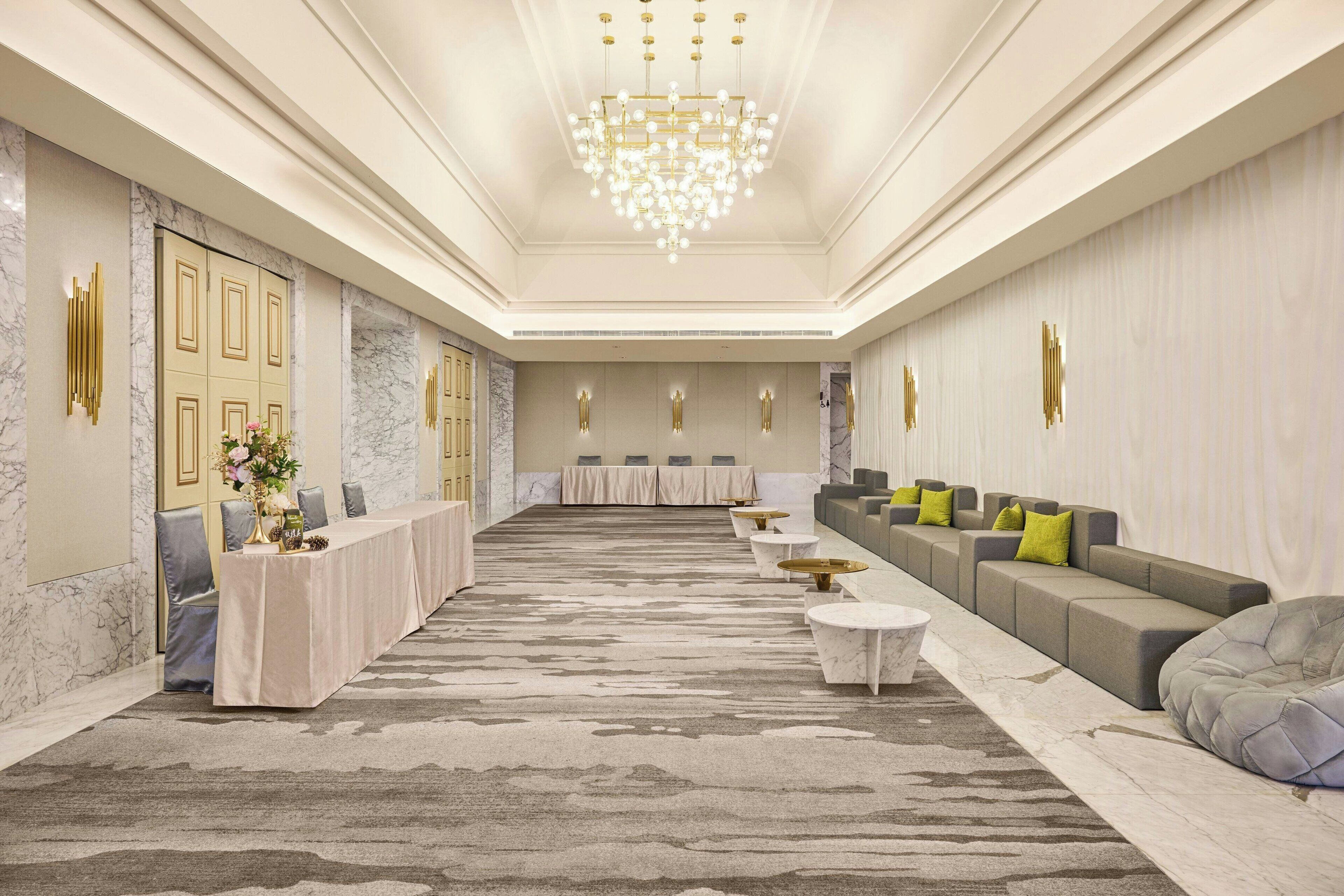 A spacious lobby with a long reception desk, seating area, and a chandelier.
