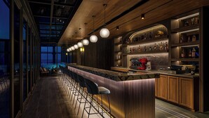 A modern bar area with a long counter, bar stools, and a wine and liquor display. - Le Méridien Taichung (Taichung)