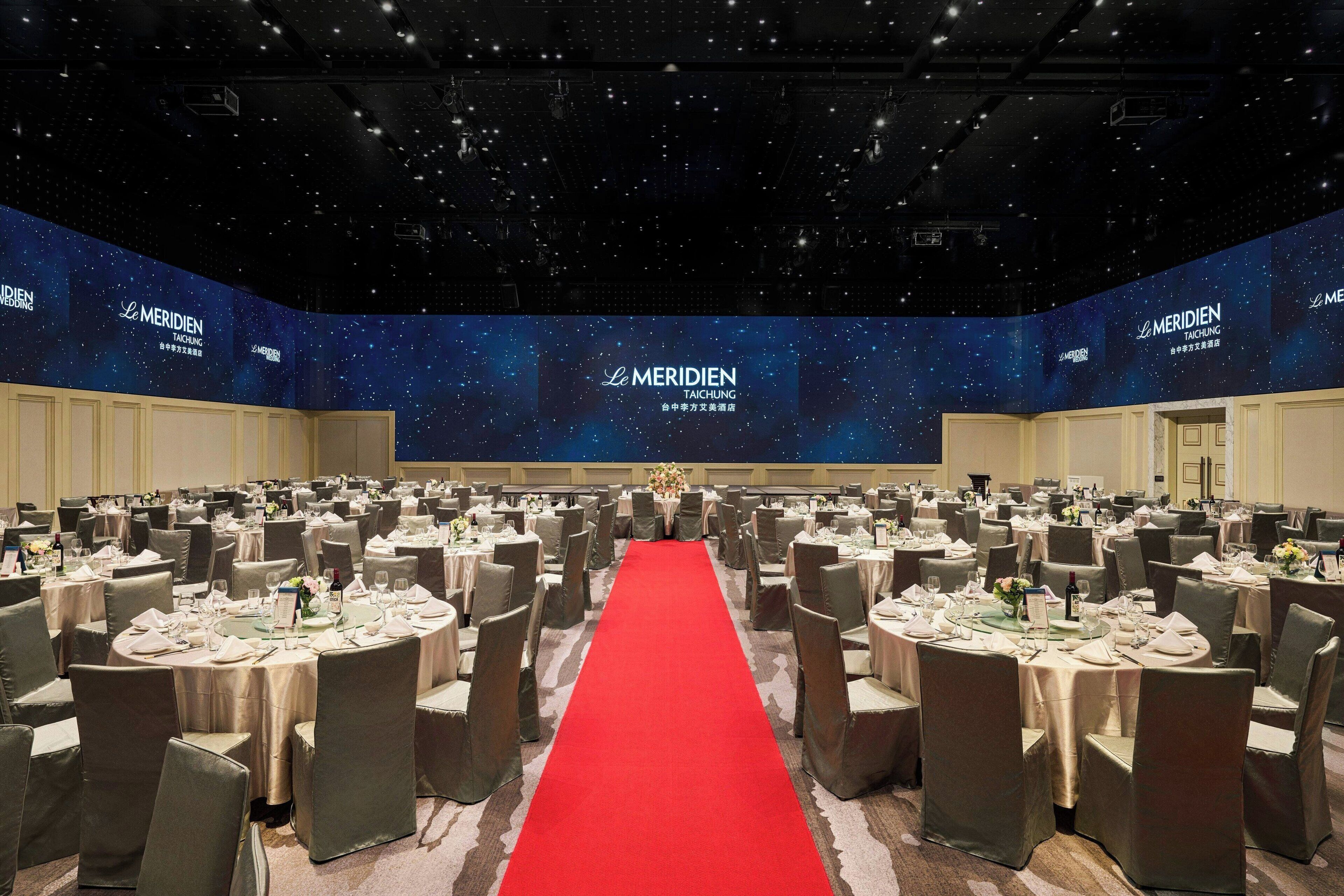 A large conference room with round tables and chairs, a red carpet, and a starry wall backdrop.