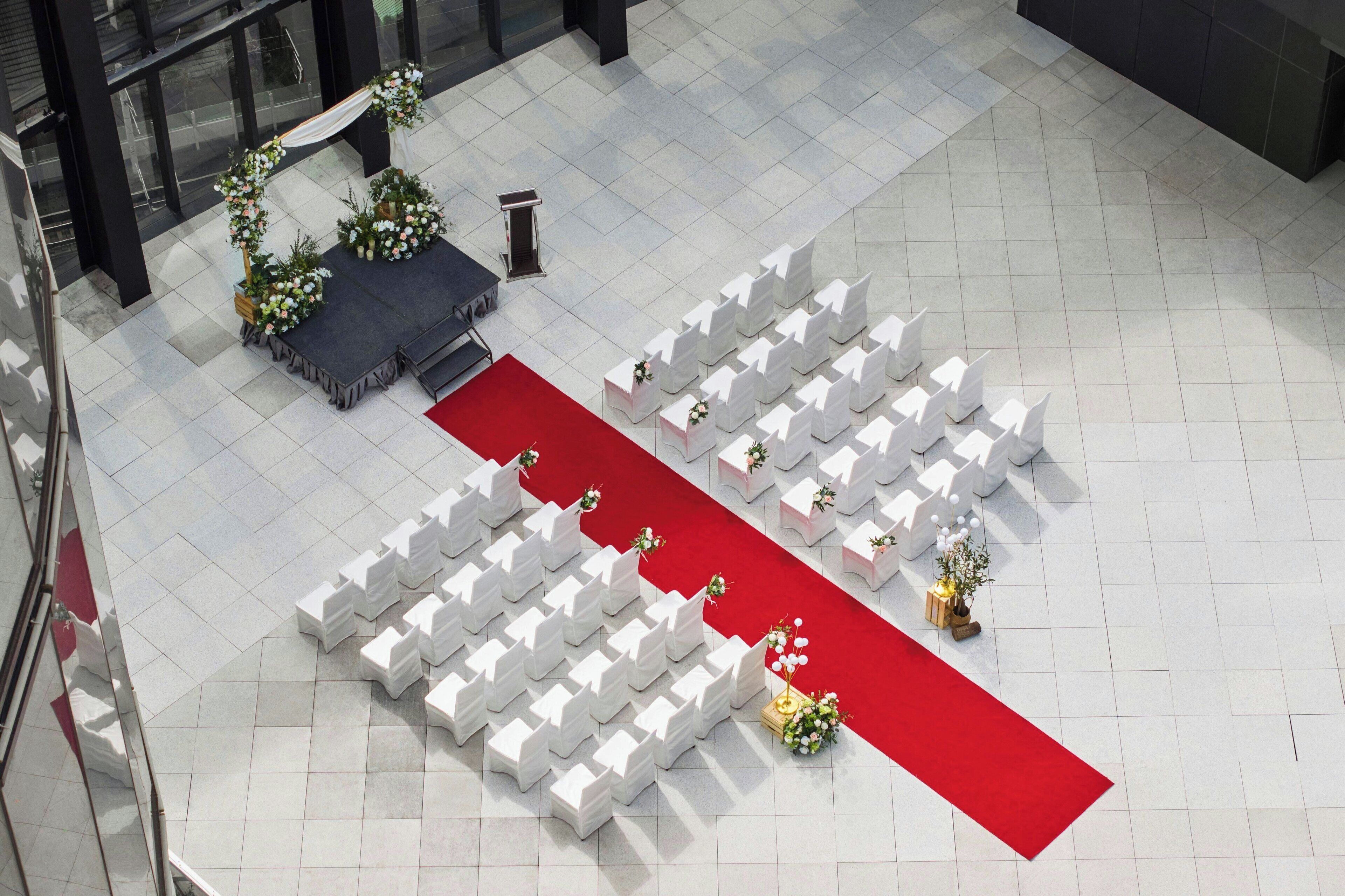 An outdoor wedding ceremony setup with white chairs arranged in rows, a red carpet, and floral decorations.