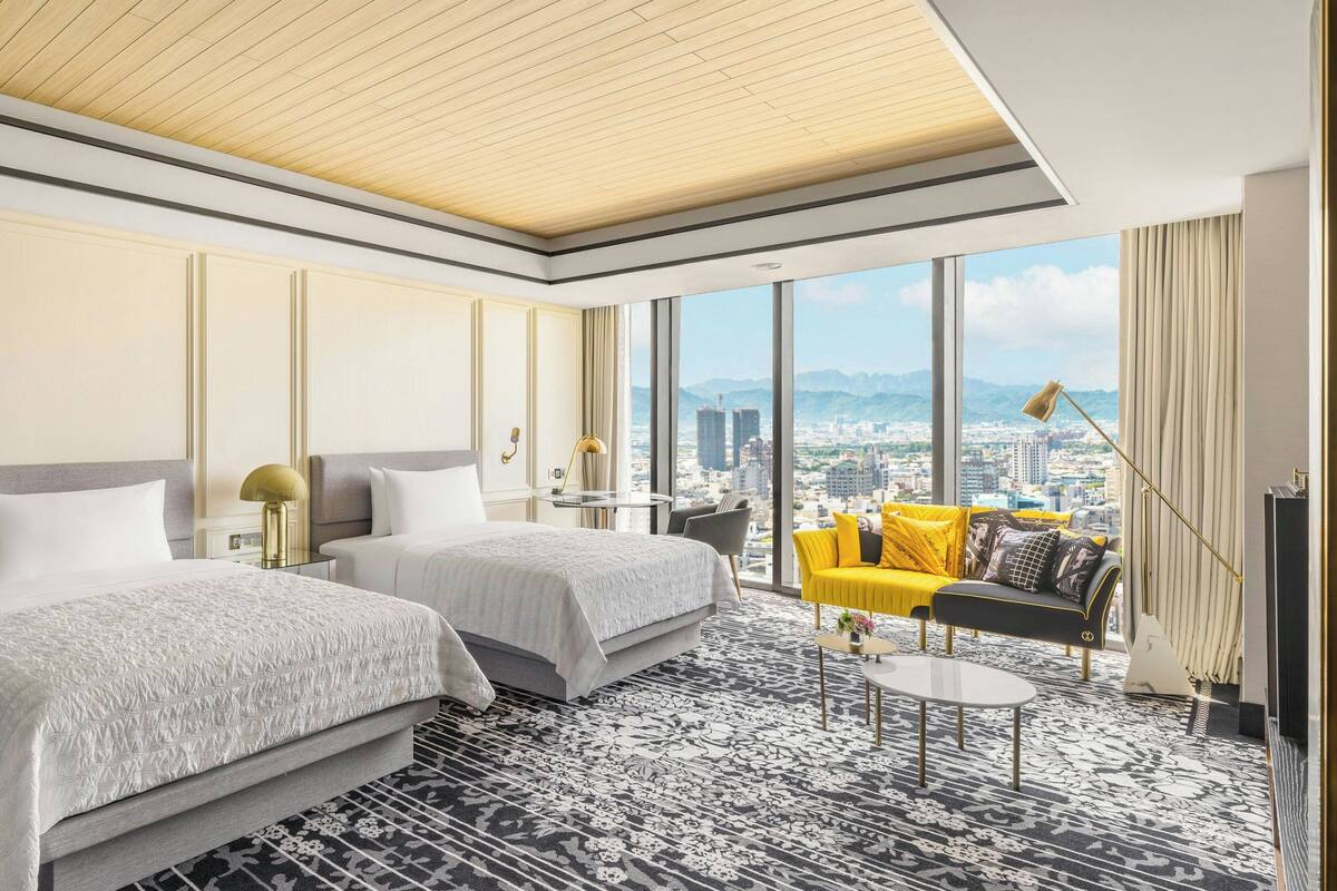 A hotel room with two beds, a sofa, a coffee table, and a city view.
