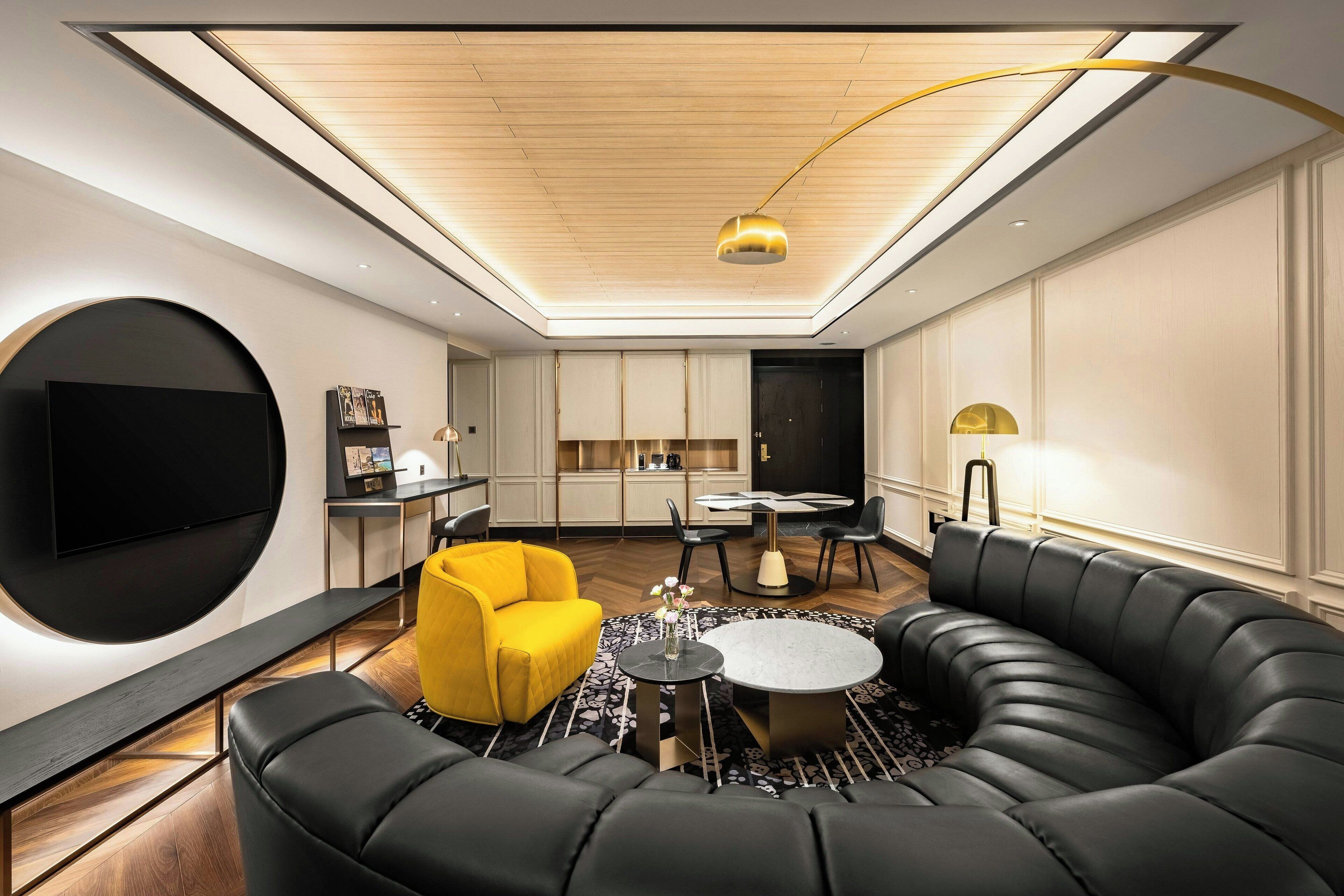 A modern living room with a black leather sofa, a yellow armchair, and a round coffee table.