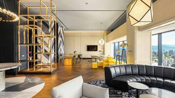 A modern living room with a black leather sofa, a white armchair, and a round coffee table. There is a geometric bookshelf and a large window offering a city view.