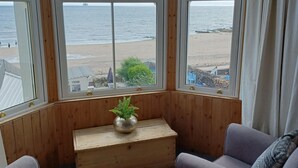 A room with a view of the beach, two grey sofas, a wooden bench, and a potted plant.