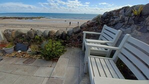 A stone bench overlooking a beach with a rocky wall and potted plants.