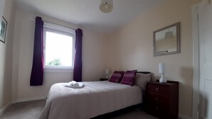A bedroom with a bed, a nightstand, a mirror, and a window with curtains.