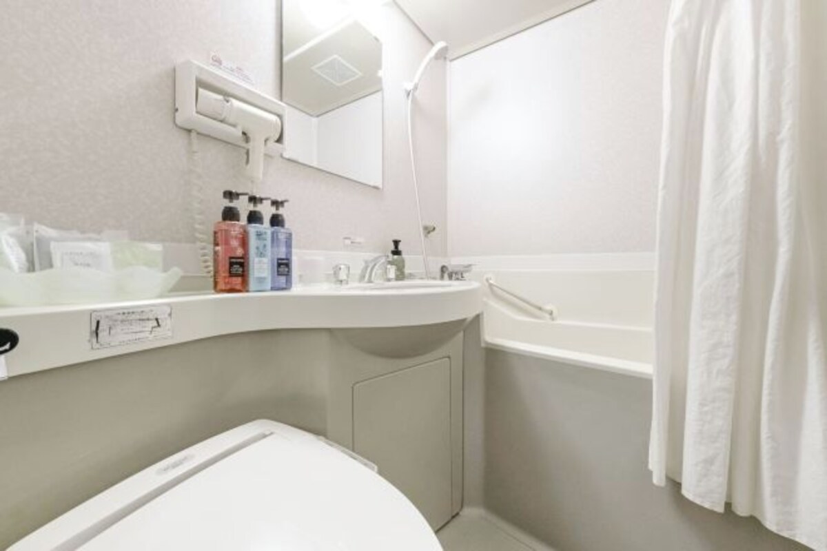 A bathroom with a white sink, mirror, and shower. There are toiletries on the sink and a towel hanging on the wall.