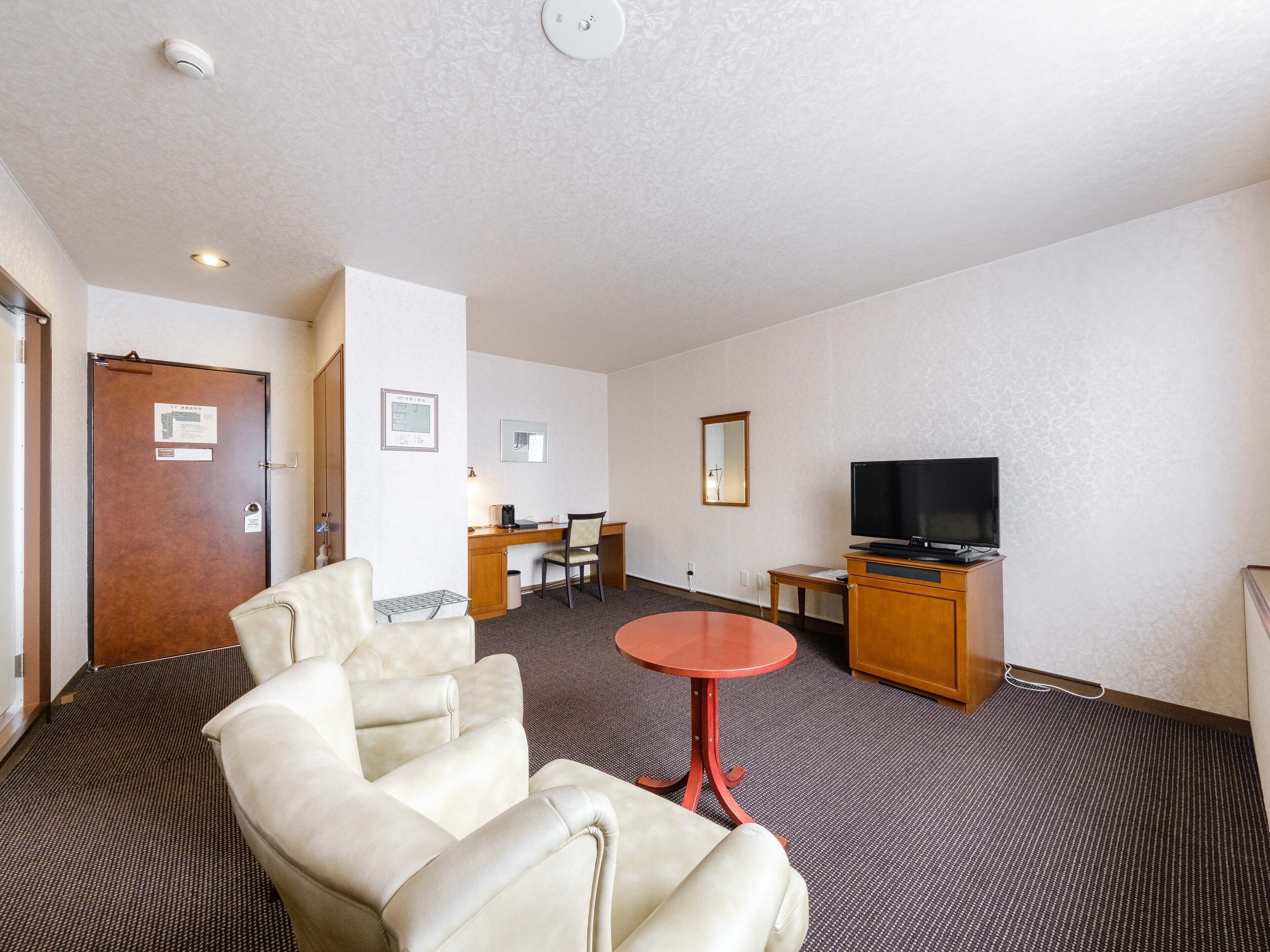 A hotel room with a seating area, a television, and a desk.