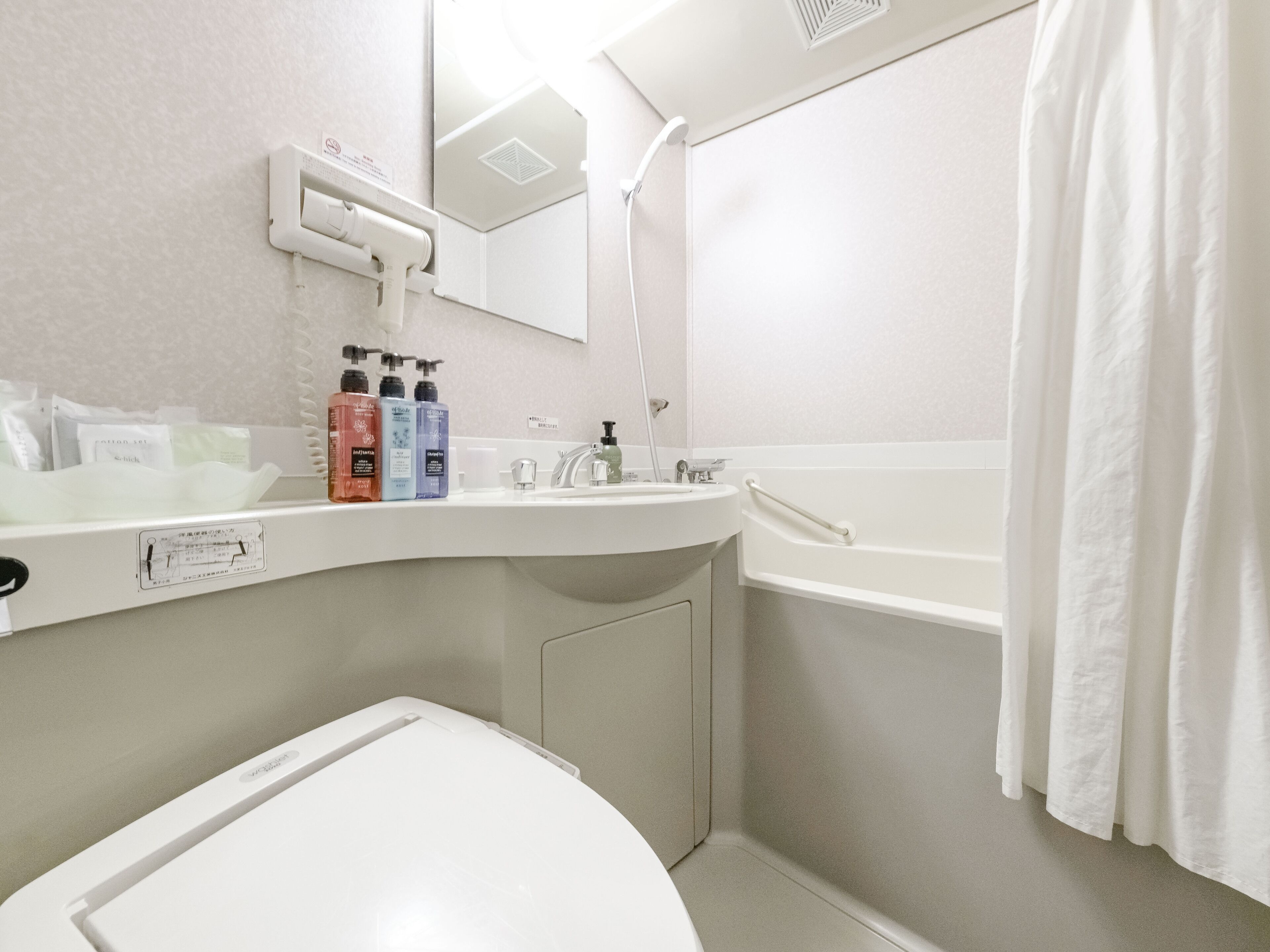 Un baño moderno con lavamanos, espejo y bañera blancos. Hay artículos de aseo en la encimera y una cortina de ducha.
