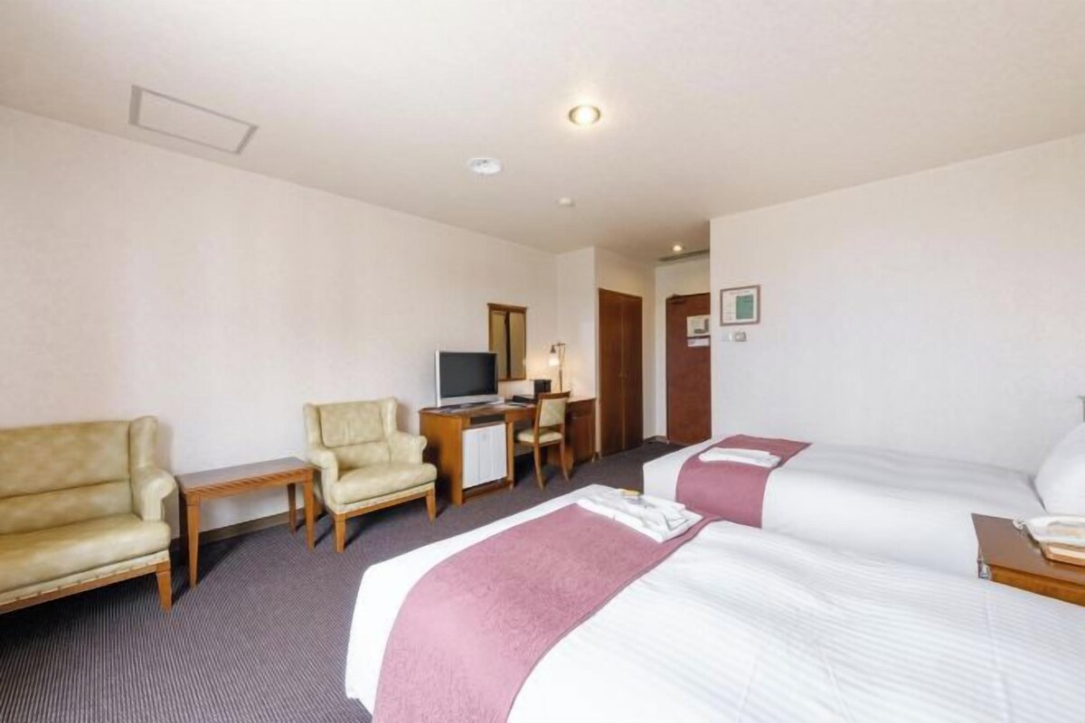 A hotel room with two beds, a desk, a television, and a chair.