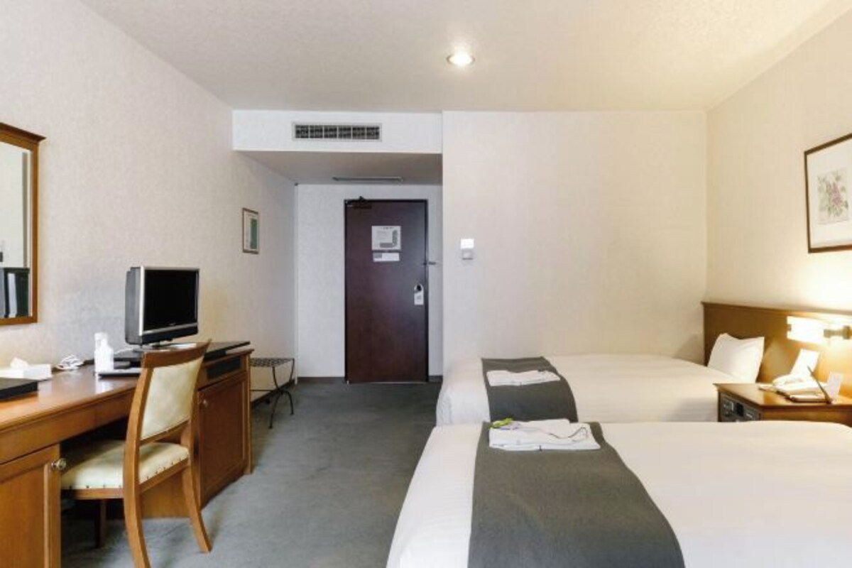 A hotel room with a desk, two beds, a TV, and a door.