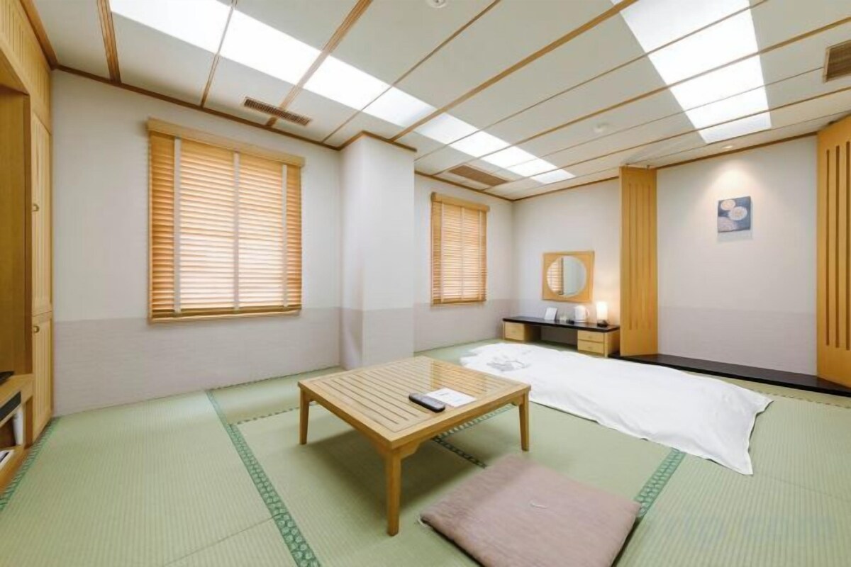 A traditional Japanese-style room with tatami flooring, a low wooden bed, a small table with a pillow, and sliding doors.