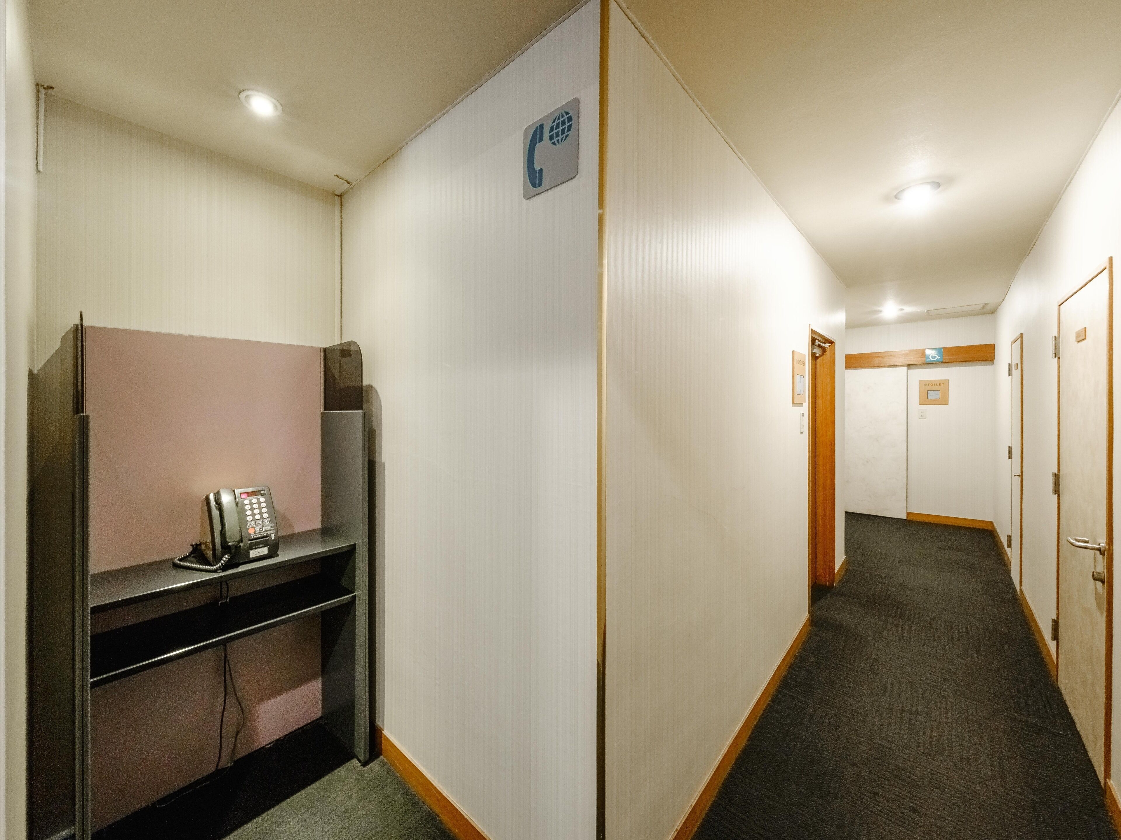 A hotel hallway with a phone on a desk, a wheelchair-accessible sign, and a door marked "Restroom".