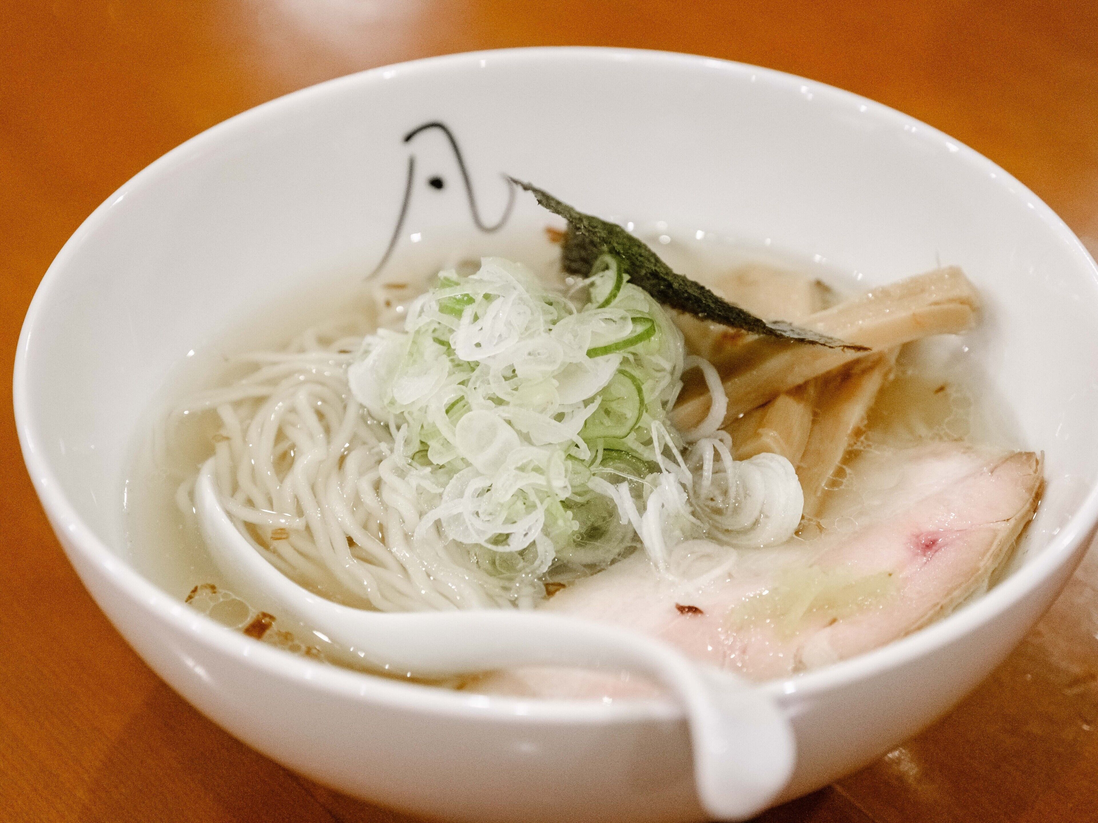 A bowl of noodle soup with sliced vegetables and a piece of meat.