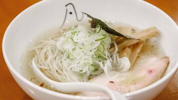 A bowl of noodle soup with sliced vegetables and a piece of meat.