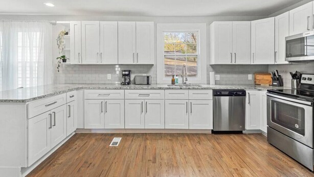 A modern kitchen with white cabinets, stainless steel appliances, and a wooden floor. - Sweet Sylvan Hills 3/2 - Ten Minutes to Airport (Atlanta)