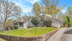 A two-story house with a front porch, a stone retaining wall, and a driveway. - Sweet Sylvan Hills 3/2 - Ten Minutes to Airport (Atlanta)